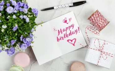 Charming birthday greeting card layout with macarons, flowers, and gift box.
