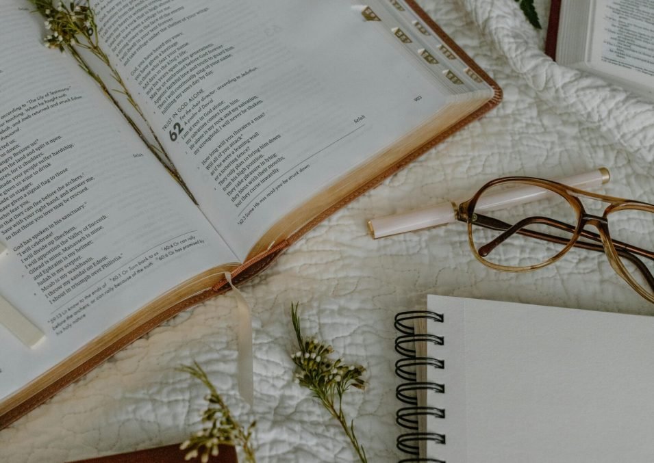pexels-photo-8383418-8383418 Cozy flat lay of an open Bible, eyeglasses, and notebooks on a white textile backdrop.